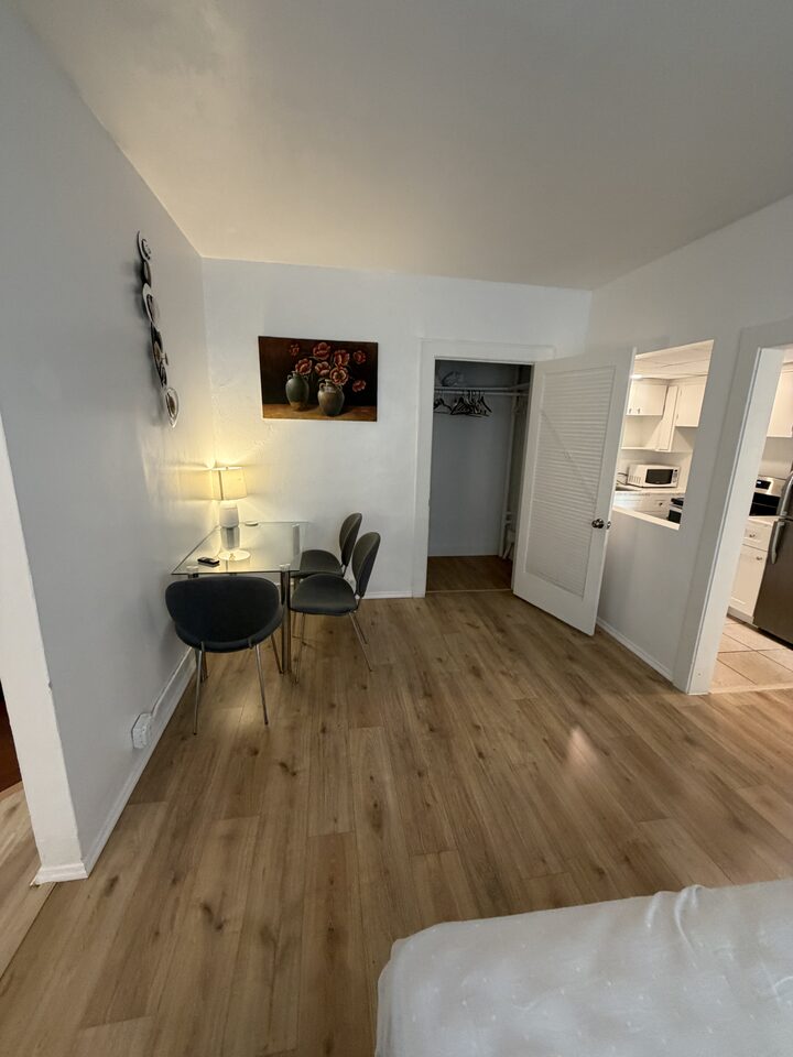 Dining area with a glass table and two chairs beside a closet, kitchen beyond
