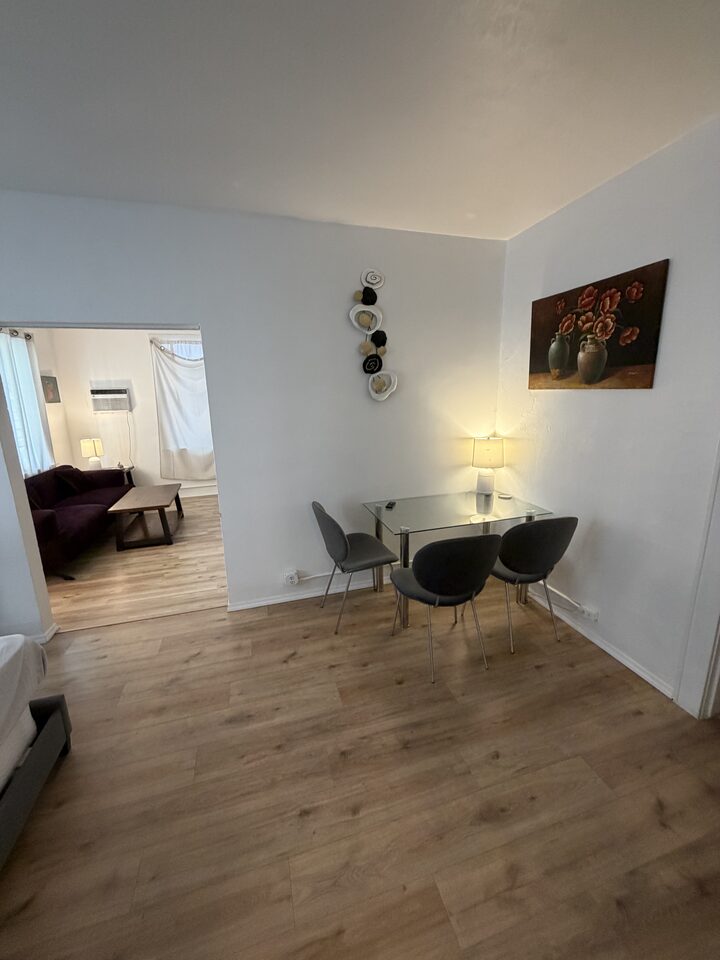 Dining area with a glass table and two chairs, living room beyond