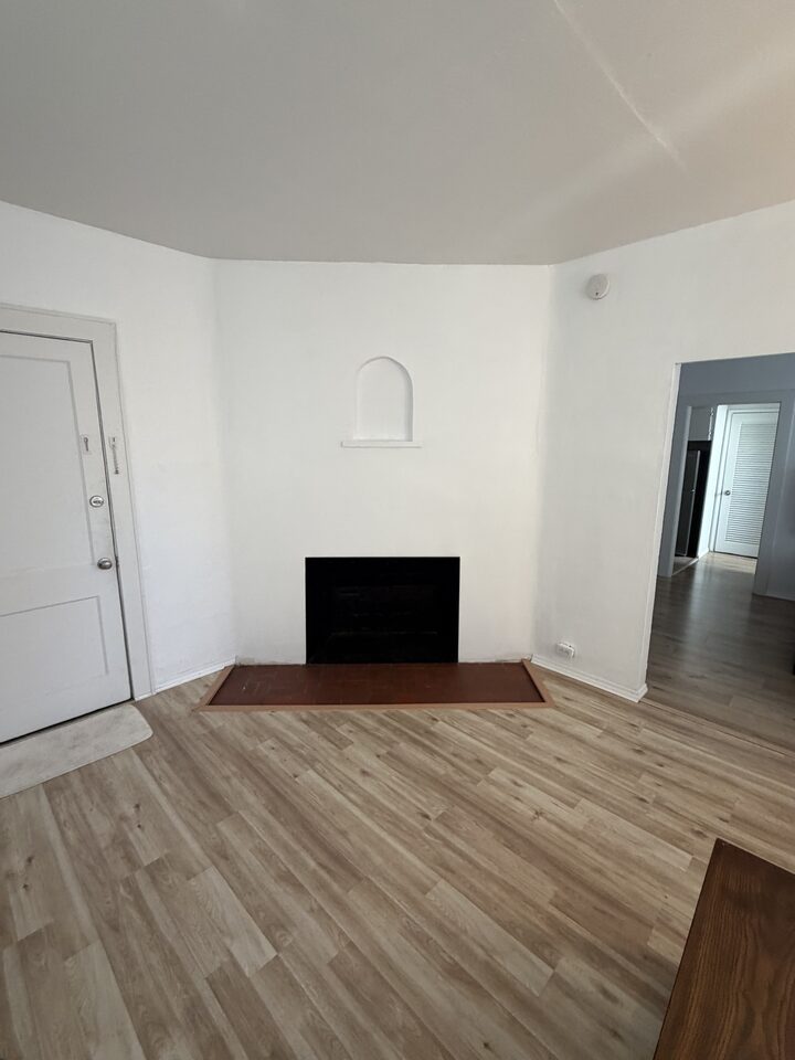 Living room with a decorative fireplace, unfurnished, showing the wood-look plank flooring