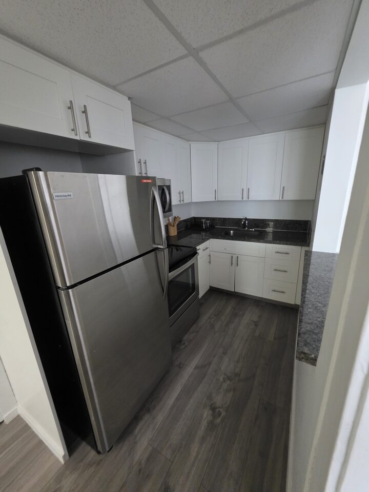 Kitchen with white shaker cabinets, a stainless steel refrigerator, an electric range with a microwave above and a dark granite countertop