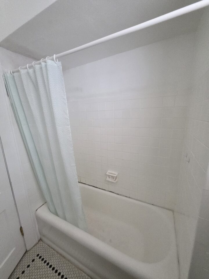 Bathtub behind a shower curtain, with white tiled walls and a hexagonal mosaic floor