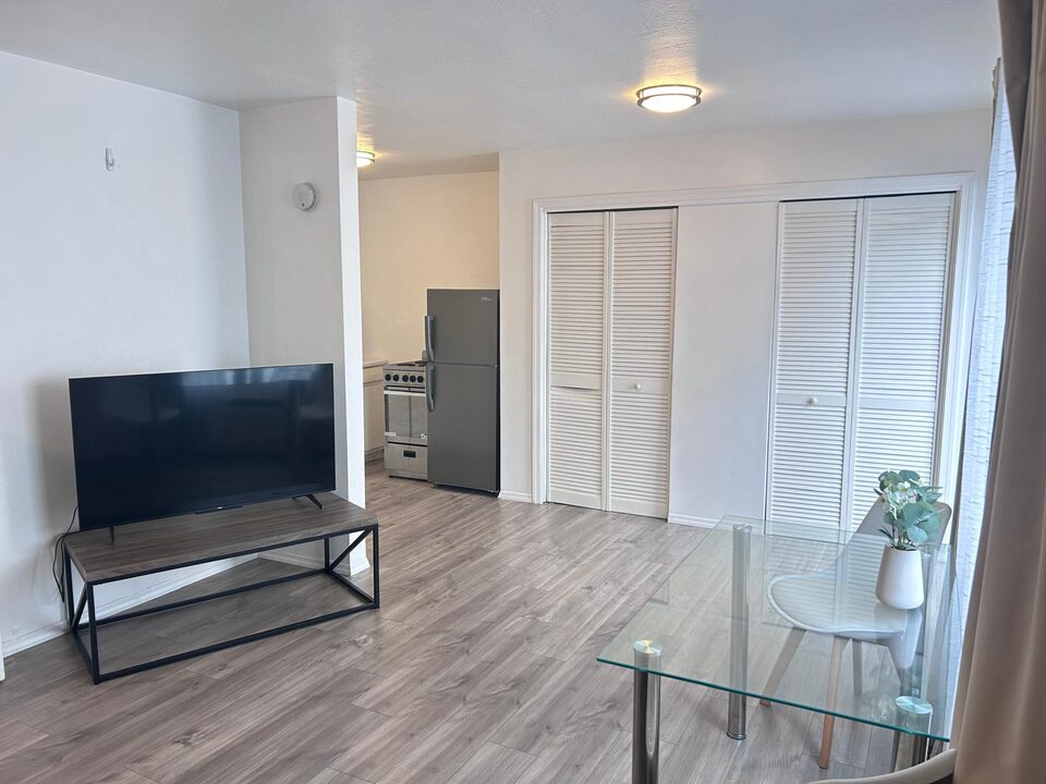 Living area with a television console and glass dining table, kitchen beyond