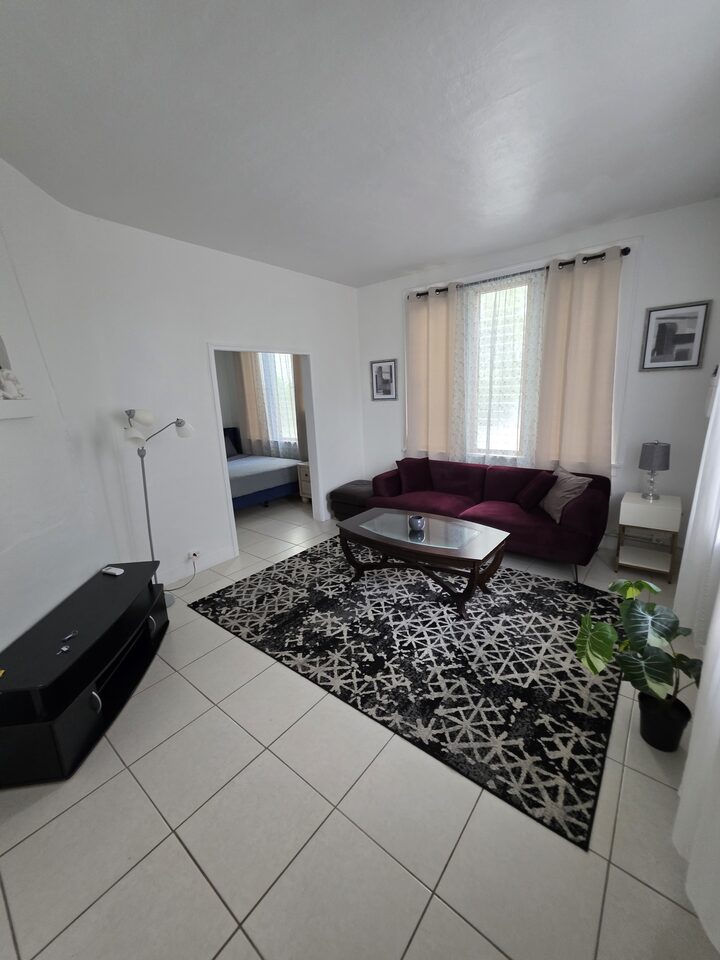 Living room looking through to the bedroom, with a television console, a floor lamp and a potted plant