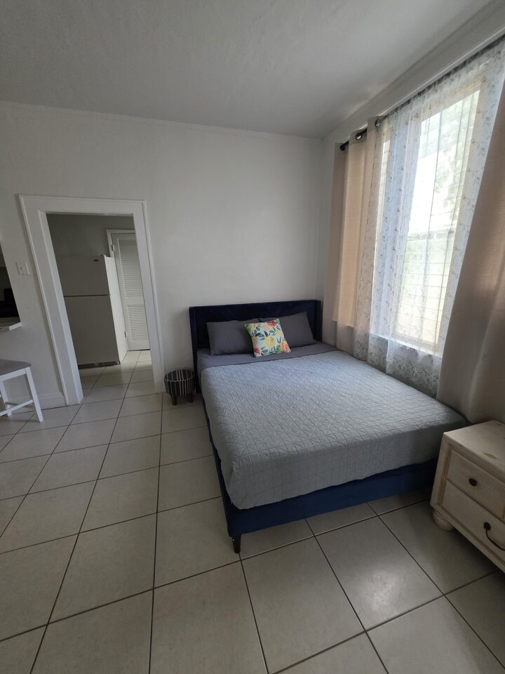 Bedroom with a navy upholstered bed, a quilted cover, a curtained window and a chest of drawers