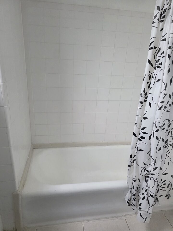 Bathtub behind a patterned shower curtain, with white tiled walls
