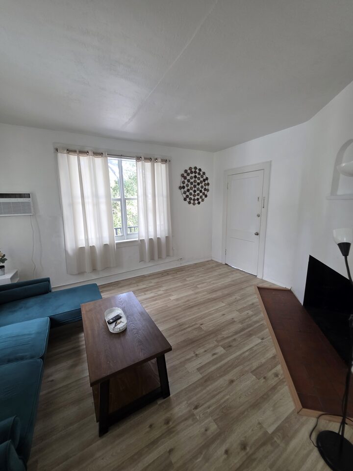 Living room looking toward the front door, with a curtained window and a raised tiled hearth