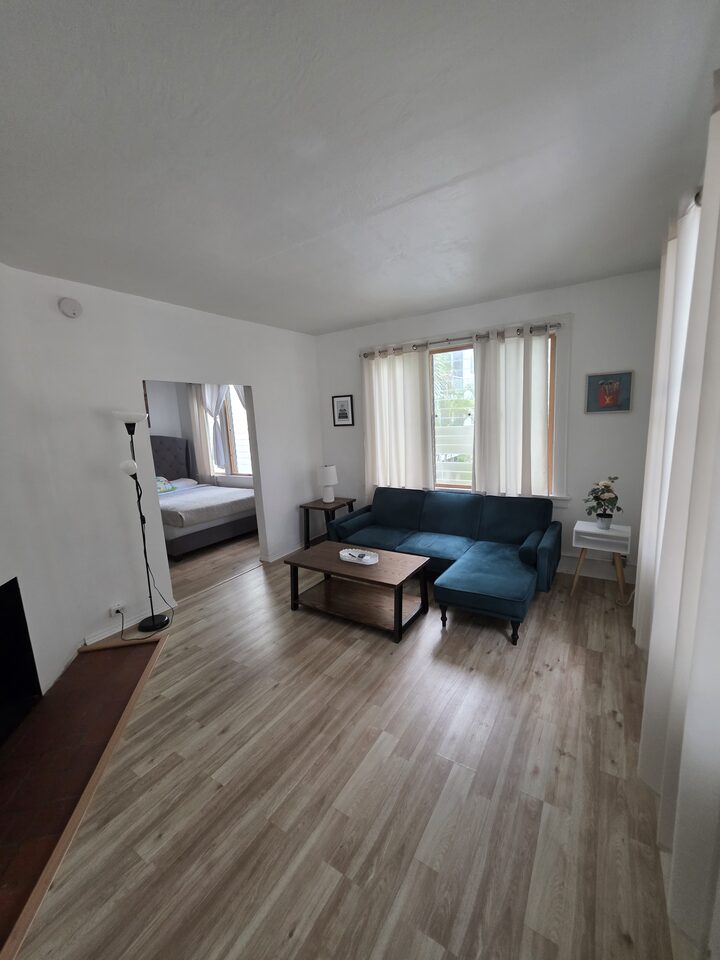 Living room looking through the opening to the bedroom, with the teal sectional and a floor lamp