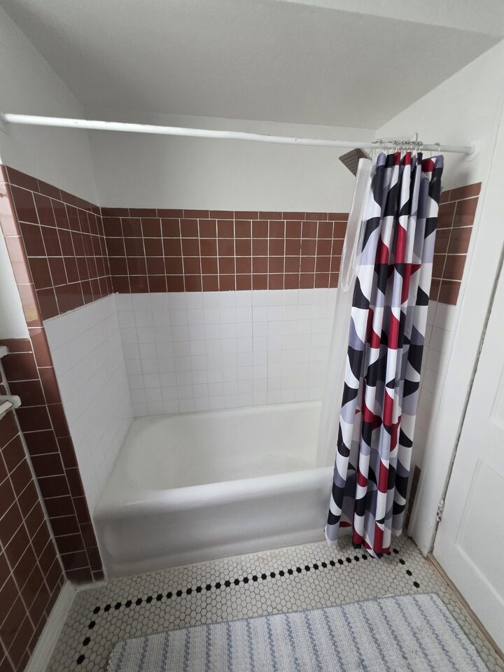 Bathtub with brown and white tiled walls, a patterned shower curtain and a hexagonal mosaic floor
