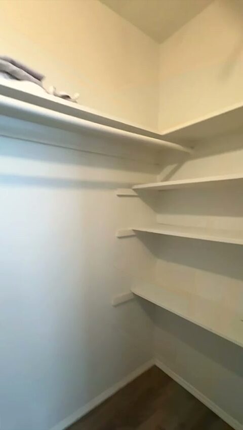Walk-in closet lined with full-width corner shelving, over wood-look plank flooring