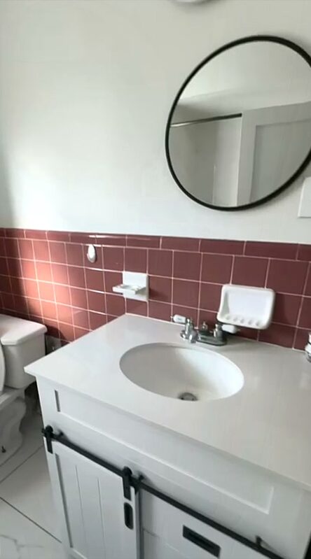 Bathroom with a round mirror over a white vanity and basin, terracotta tiled wainscot and a toilet beside the vanity