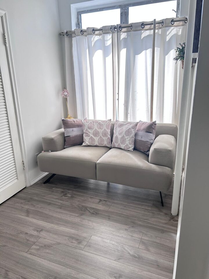 Living area with a sofa beneath a curtained window and wood-look plank flooring
