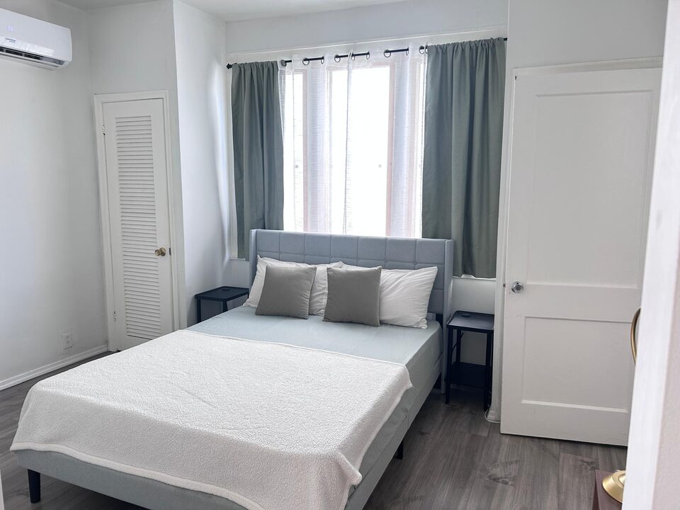 Bedroom with a queen bed, louvered closet doors and a wall air conditioning unit