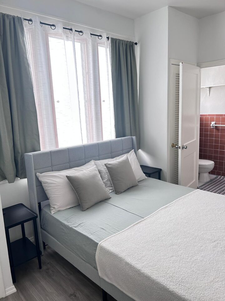Bedroom with an upholstered headboard and the tiled bathroom beyond