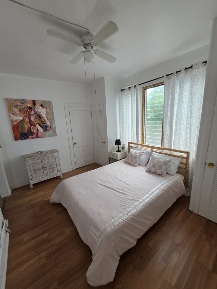 Bedroom with a wooden bed frame, a ceiling fan, a curtained window and a painted cabinet