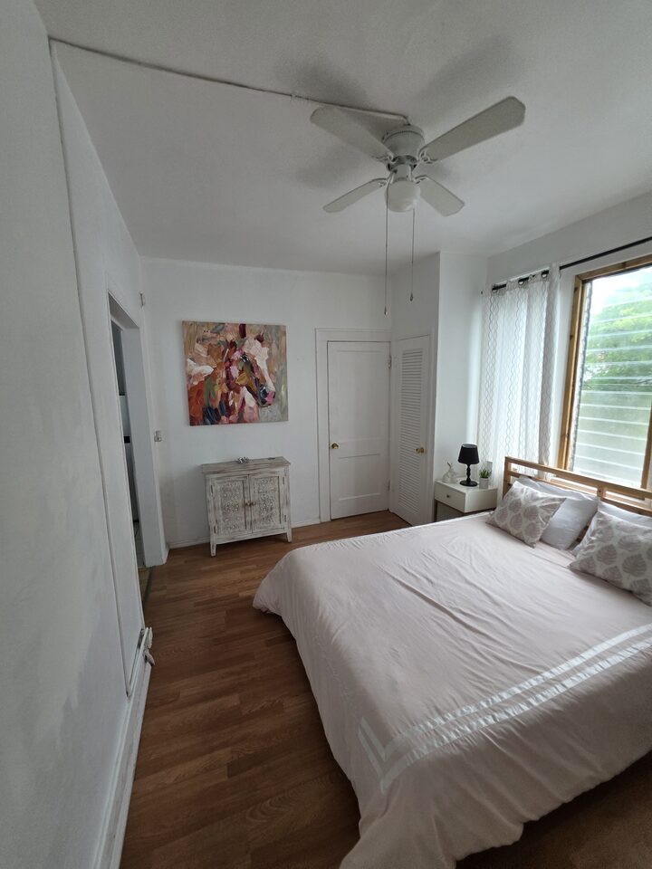 Bedroom seen from the doorway, with the bed, a painted cabinet and louvered closet doors