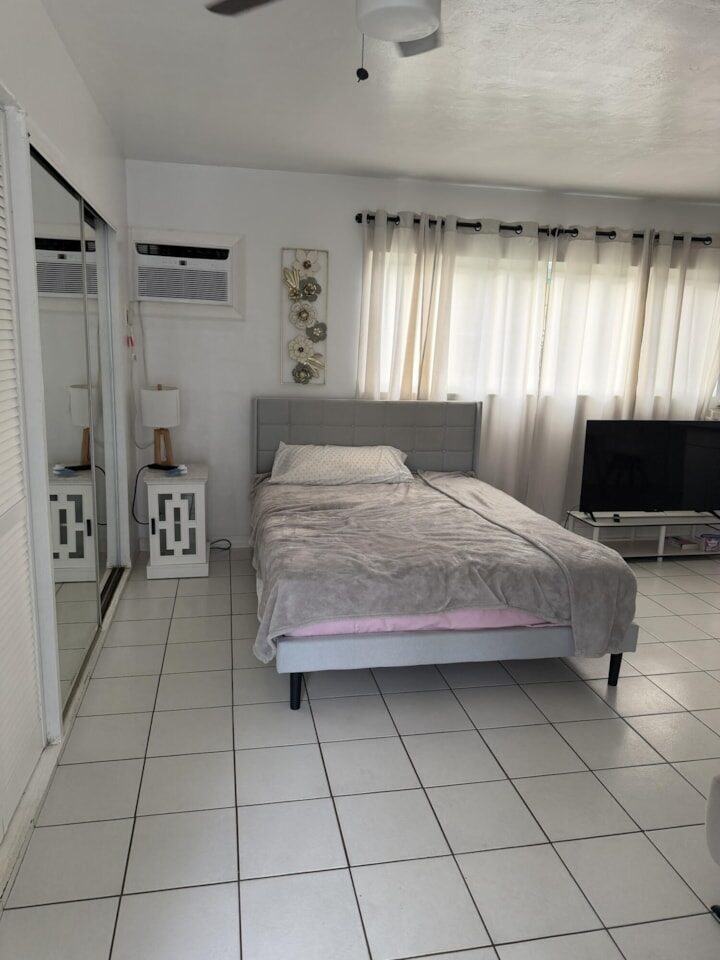 Bedroom with a queen bed, mirrored closet doors, wall air conditioning unit and white tile floors