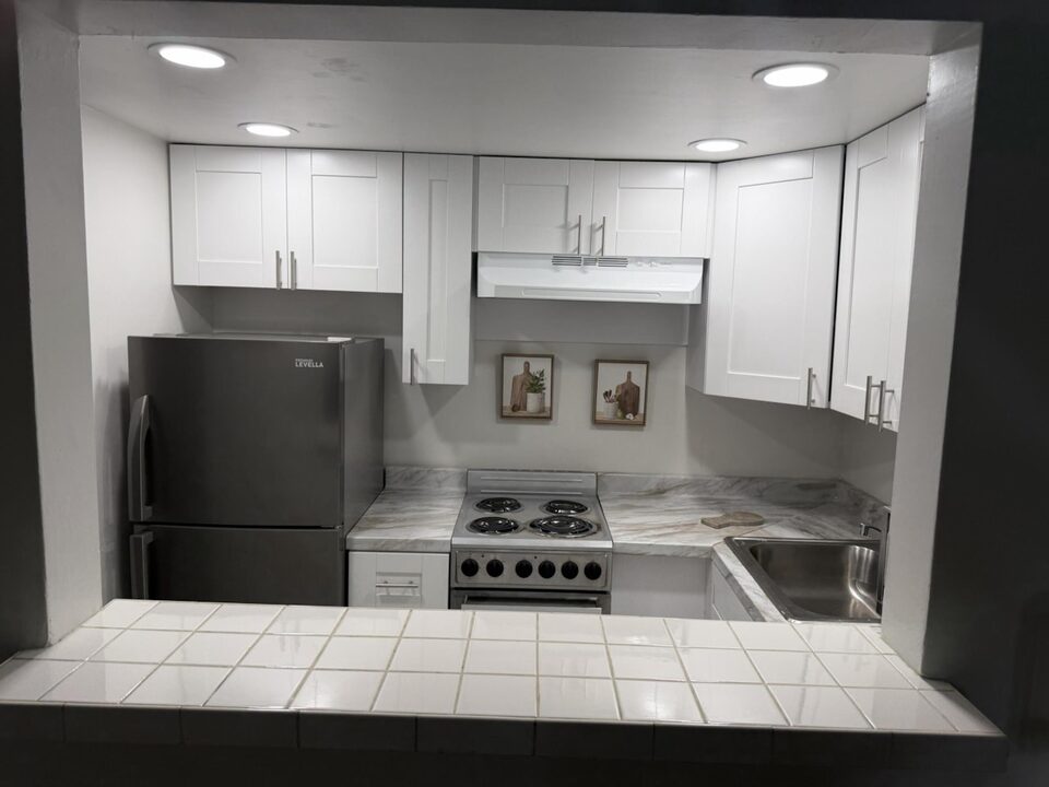 Kitchen behind a tiled pass-through counter, with white cabinets, range and stainless sink
