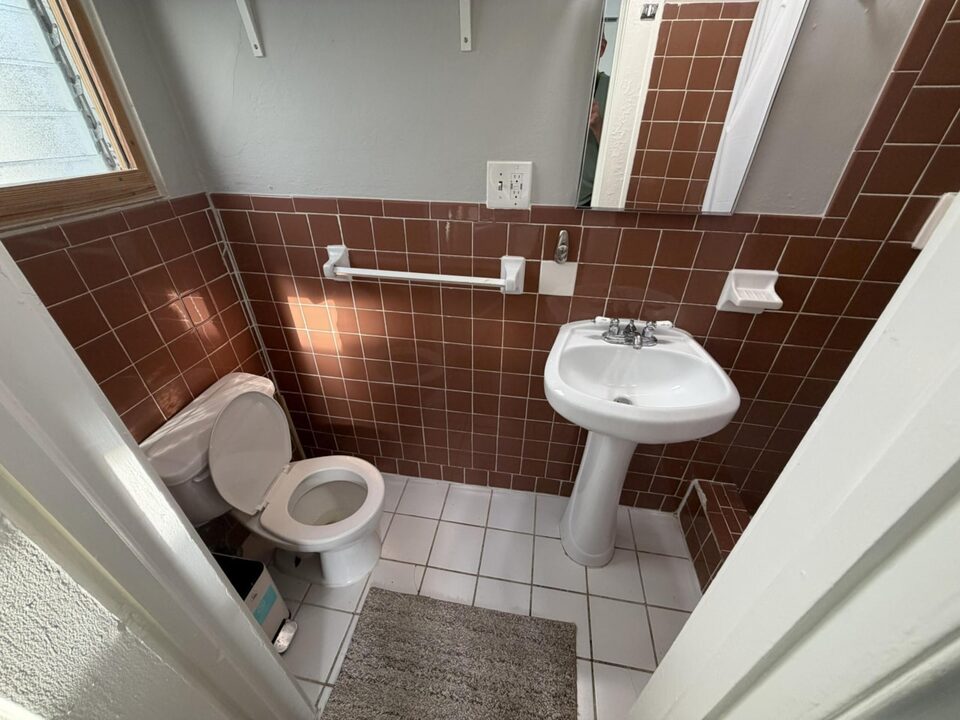 Bathroom with terracotta tiled walls, pedestal sink and toilet