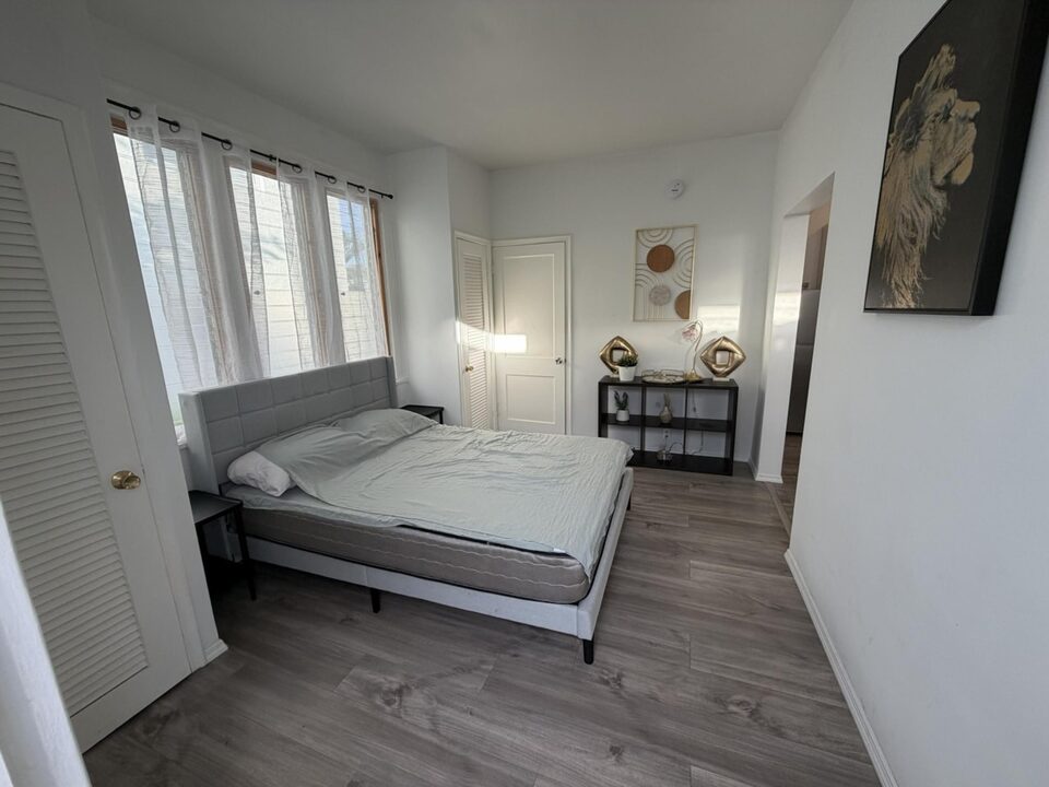 Bedroom with a queen bed, louvered closet doors, plank flooring and a curtained window