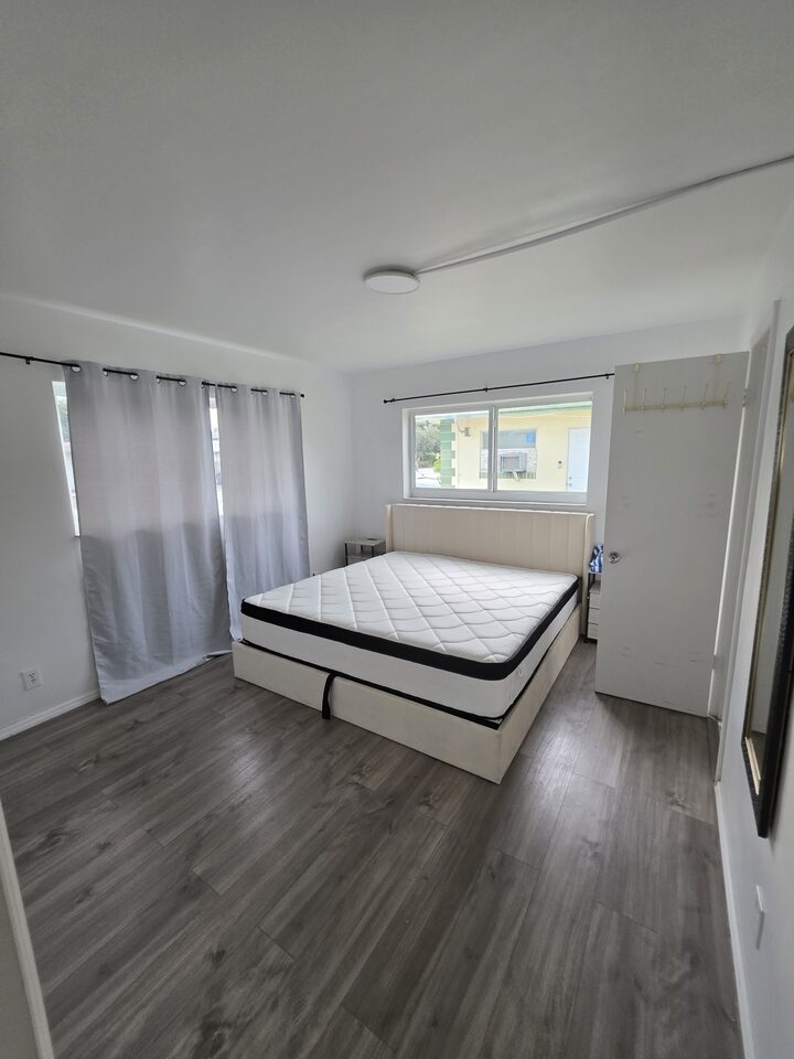 Bedroom with an upholstered headboard, curtained windows and a closet door, the mattress not yet made up