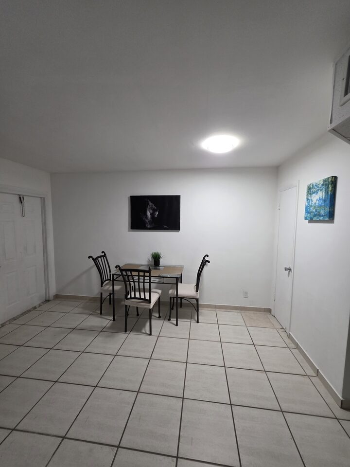 Dining area with a glass table and four chairs on white tile floors, beside the closet doors