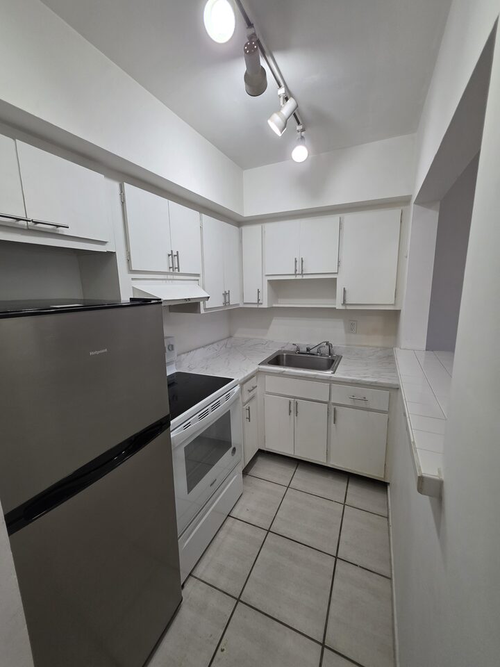 Kitchen with white cabinets, a refrigerator, an electric range, a stainless steel sink and a marble-look countertop