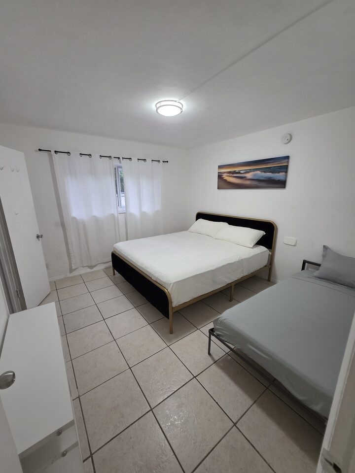 Bedroom with two beds, a curtained window and a wardrobe, on white tile floors
