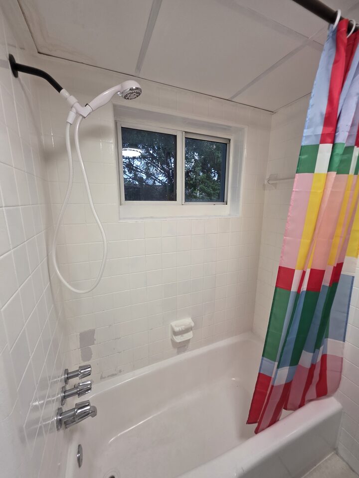 Bathtub with a handheld shower, white tiled walls and a window