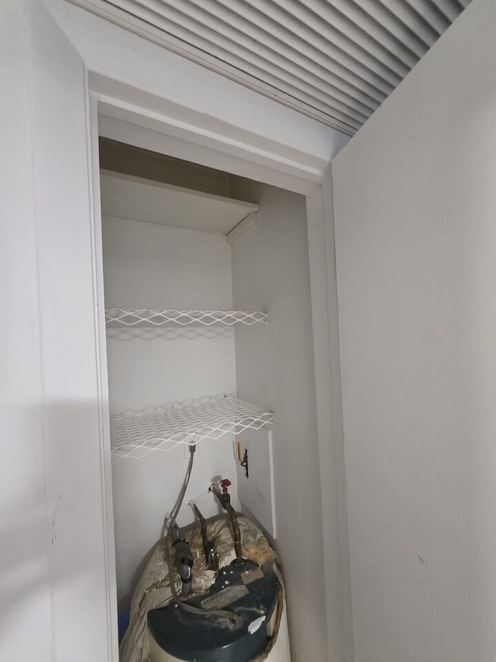 Utility closet housing the water heater, with shelving above