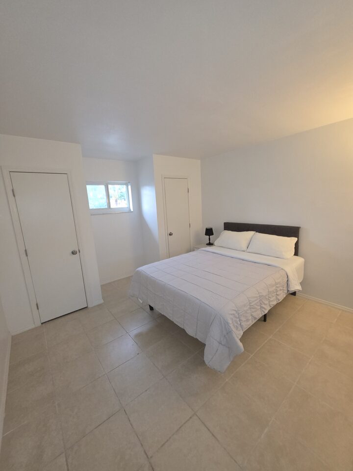 Bedroom with a dark upholstered headboard, white bedding, a window and two closet doors