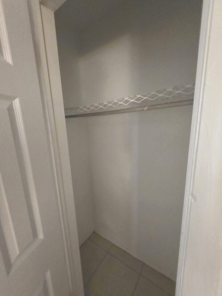 Closet with a wire shelf and hanging rail, its panelled door standing open