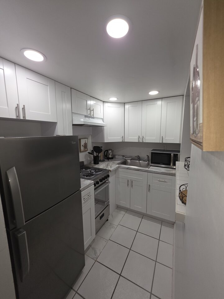 Galley kitchen with white cabinets, a refrigerator, an electric range, a microwave and a stainless steel sink