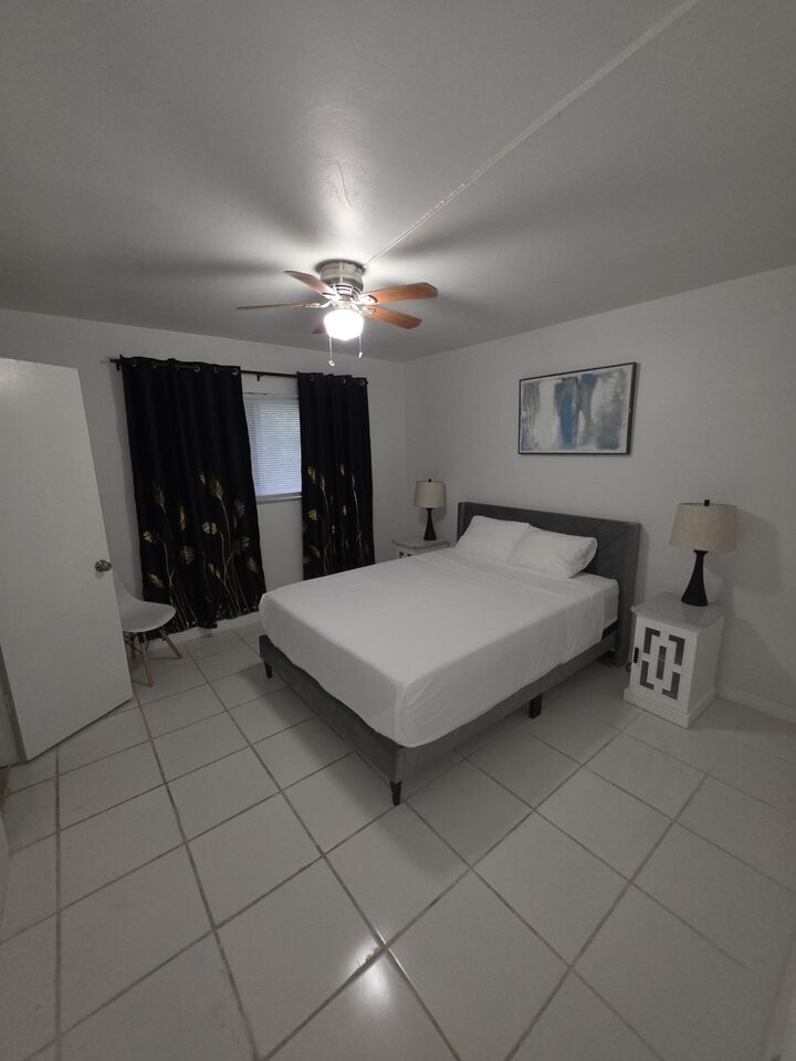 Bedroom with an upholstered bed, a ceiling fan, blackout curtains and a bedside lamp on each side