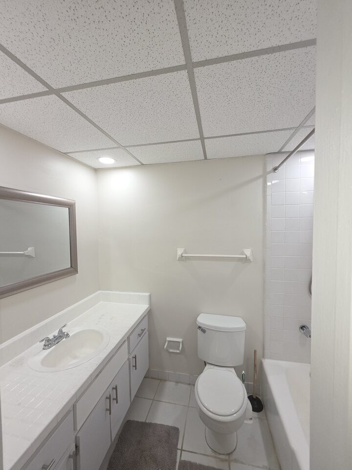 Bathroom with a vanity, a mirror, a toilet and a tub with a tiled surround