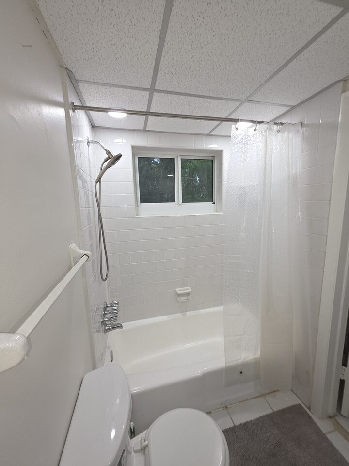 Bathtub with a handheld shower, white tiled walls and a window
