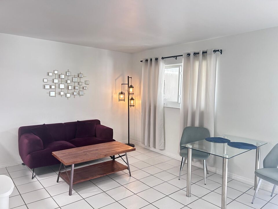 Living room with a burgundy sofa, wood coffee table and glass dining table beside a curtained window