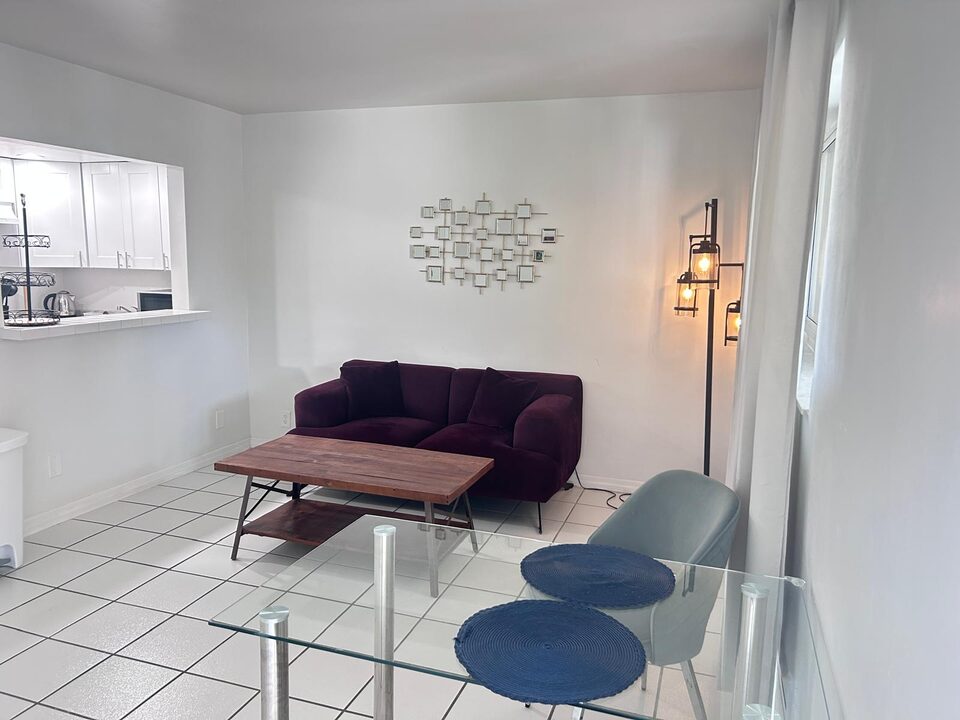 Living area looking toward the kitchen pass-through, with a floor lamp and white tile floors