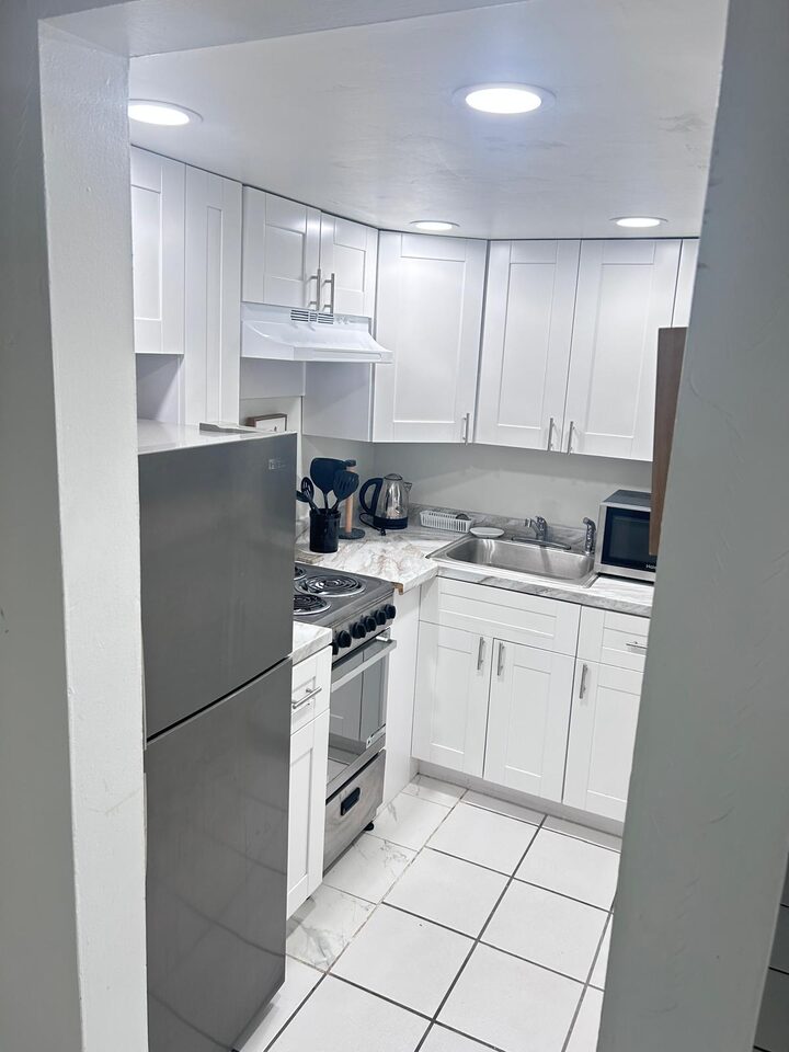 Kitchen seen from the doorway, with a stainless steel refrigerator, electric range and white cabinets
