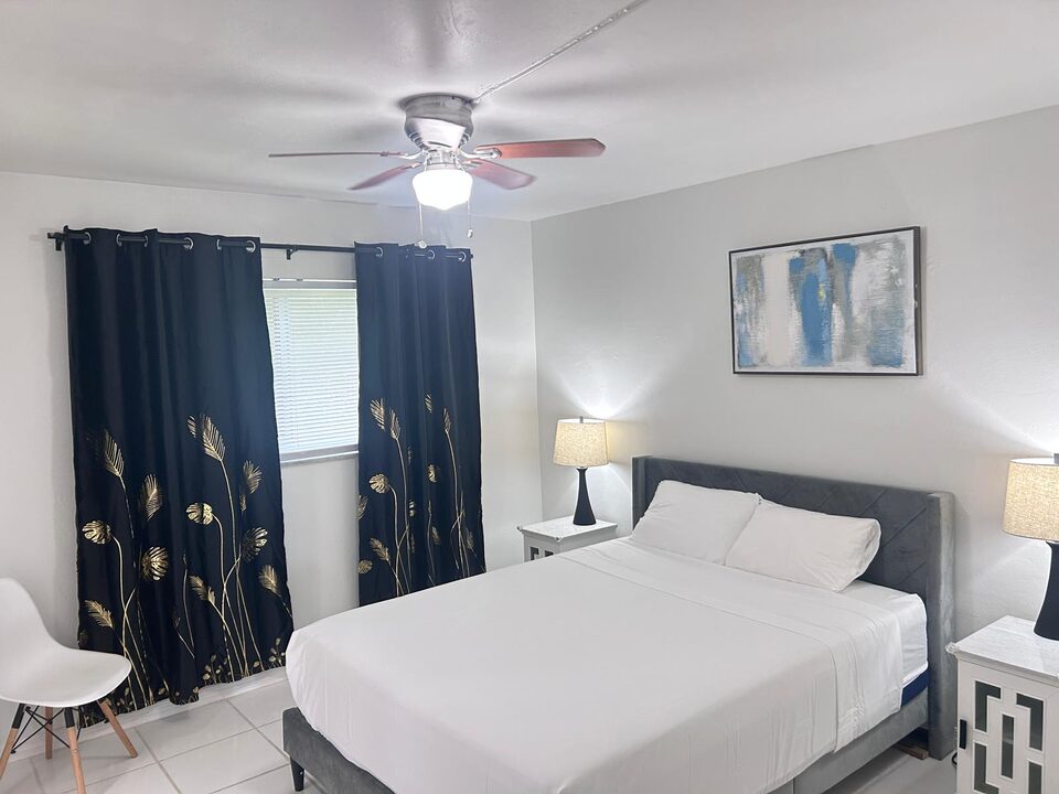 Bedroom with a ceiling fan, navy curtains and a window over white tile floors