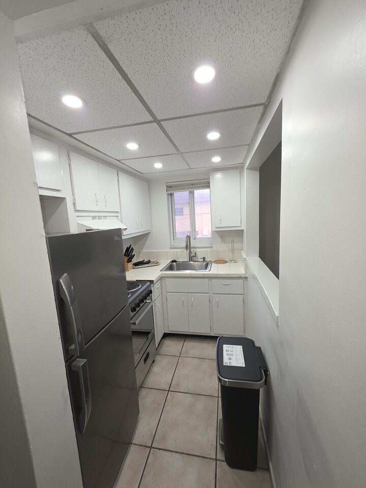 Galley kitchen seen from the hallway, with a stainless steel sink under the window, the range and refrigerator along one wall and the pass-through to the living room