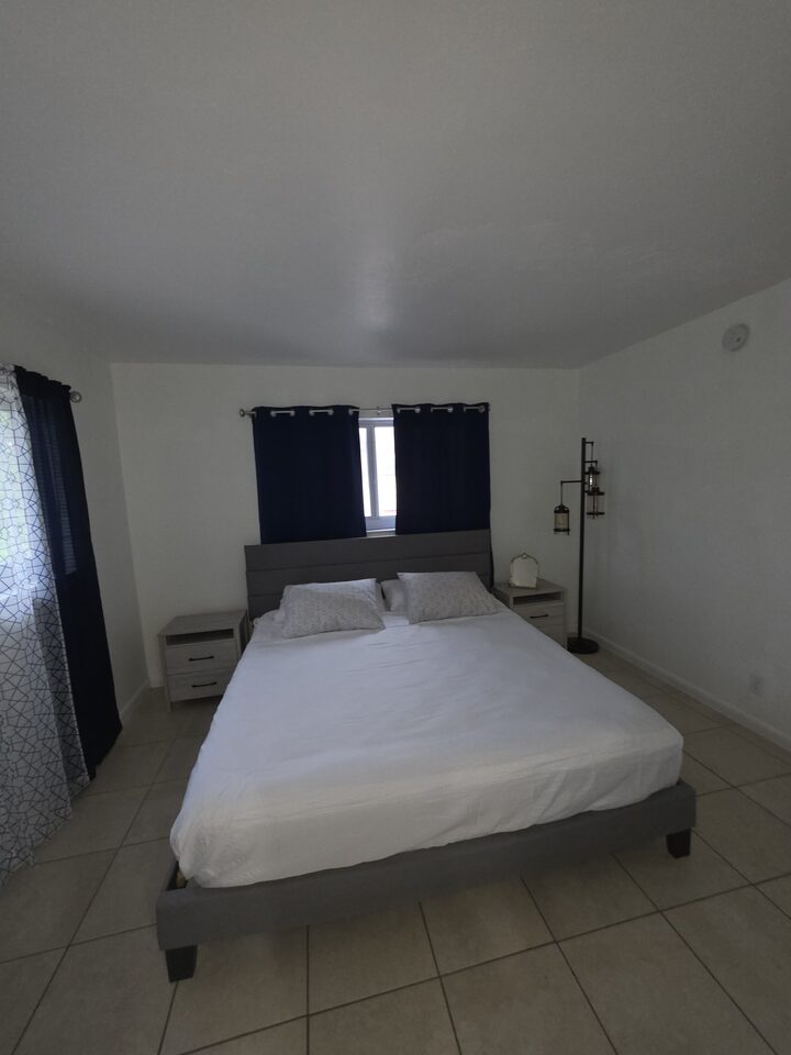 Bedroom with a king bed, a grey upholstered headboard, navy curtains at the window, a nightstand on each side and a standing lamp