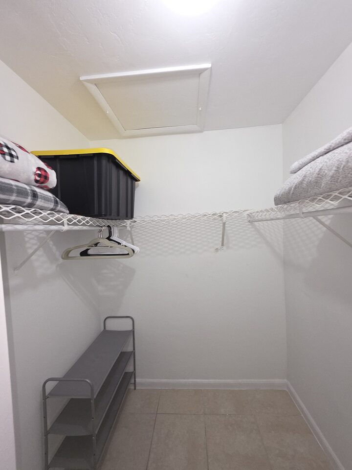 Walk-in closet with wire shelving, two hanging rails, a shoe rack and an attic hatch in the ceiling