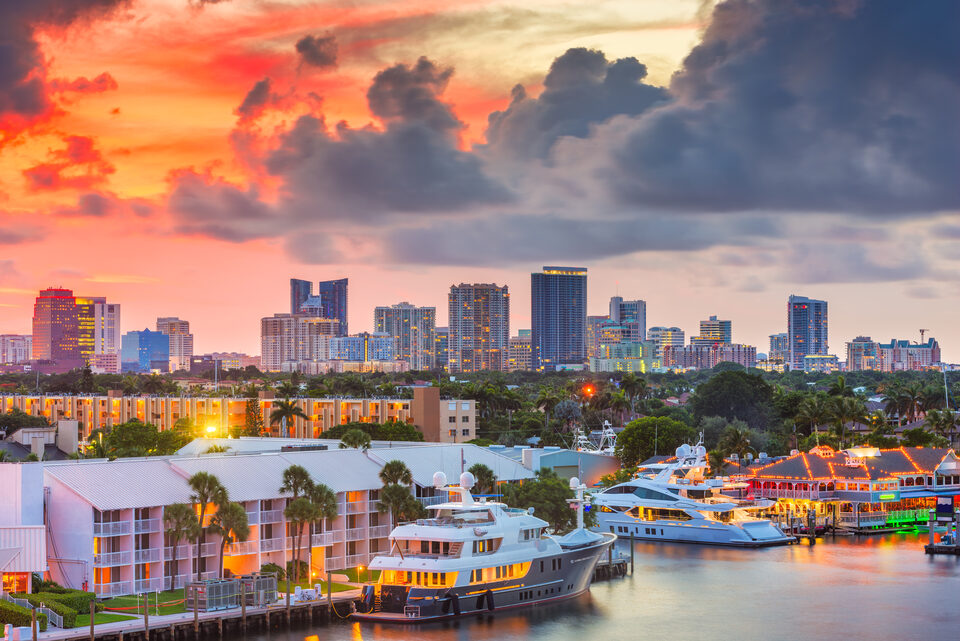 The downtown Fort Lauderdale skyline under a red sunset, with yachts moored on the water below