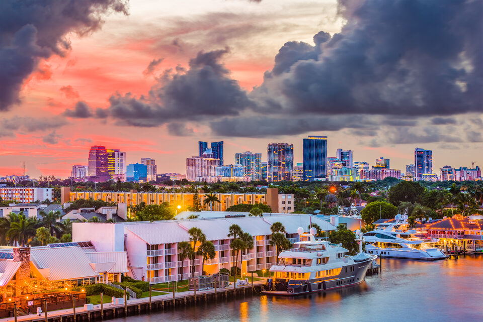 The downtown Fort Lauderdale skyline at dusk seen across the waterway, with yachts moored along the quay